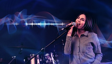 Image of Young singer with microphone recording song in studio, color toned. Audio waveforms near her