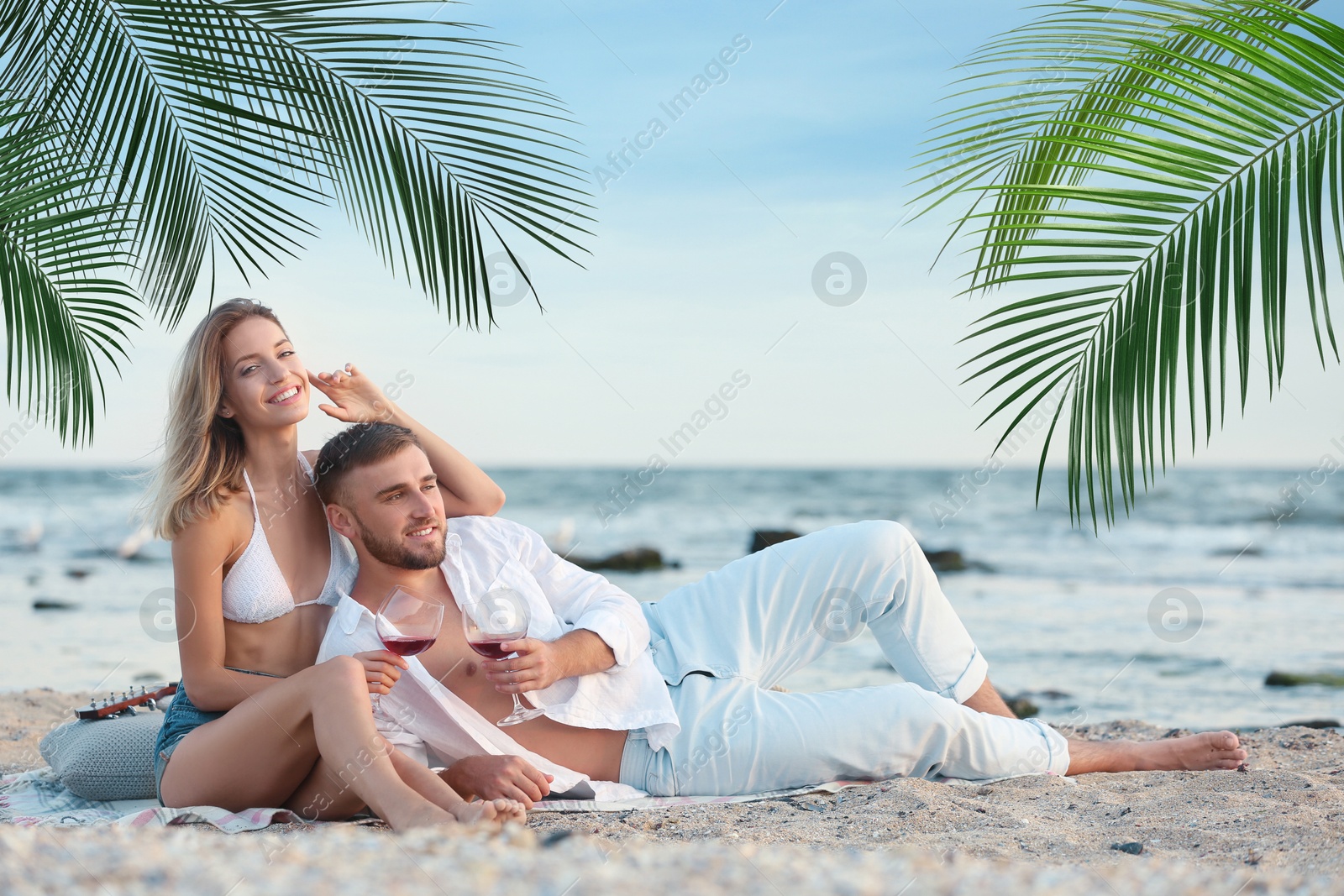 Image of Happy honeymooners relaxing under palm leaves on tropical beach