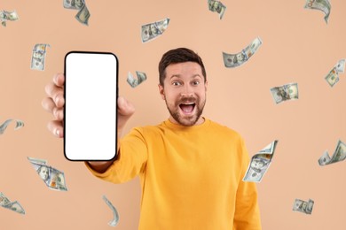 Happy man showing mobile phone with empty screen under money rain on dark beige background