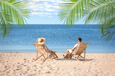 Couple relaxing on deck chairs under palm leaves on tropical beach