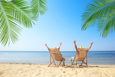 Couple relaxing on deck chairs under palm leaves on tropical beach