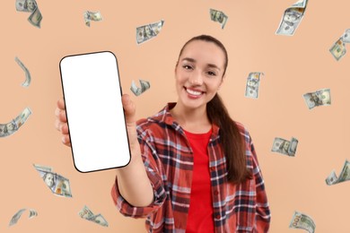 Image of Happy woman showing mobile phone with empty screen under money rain on dark beige background