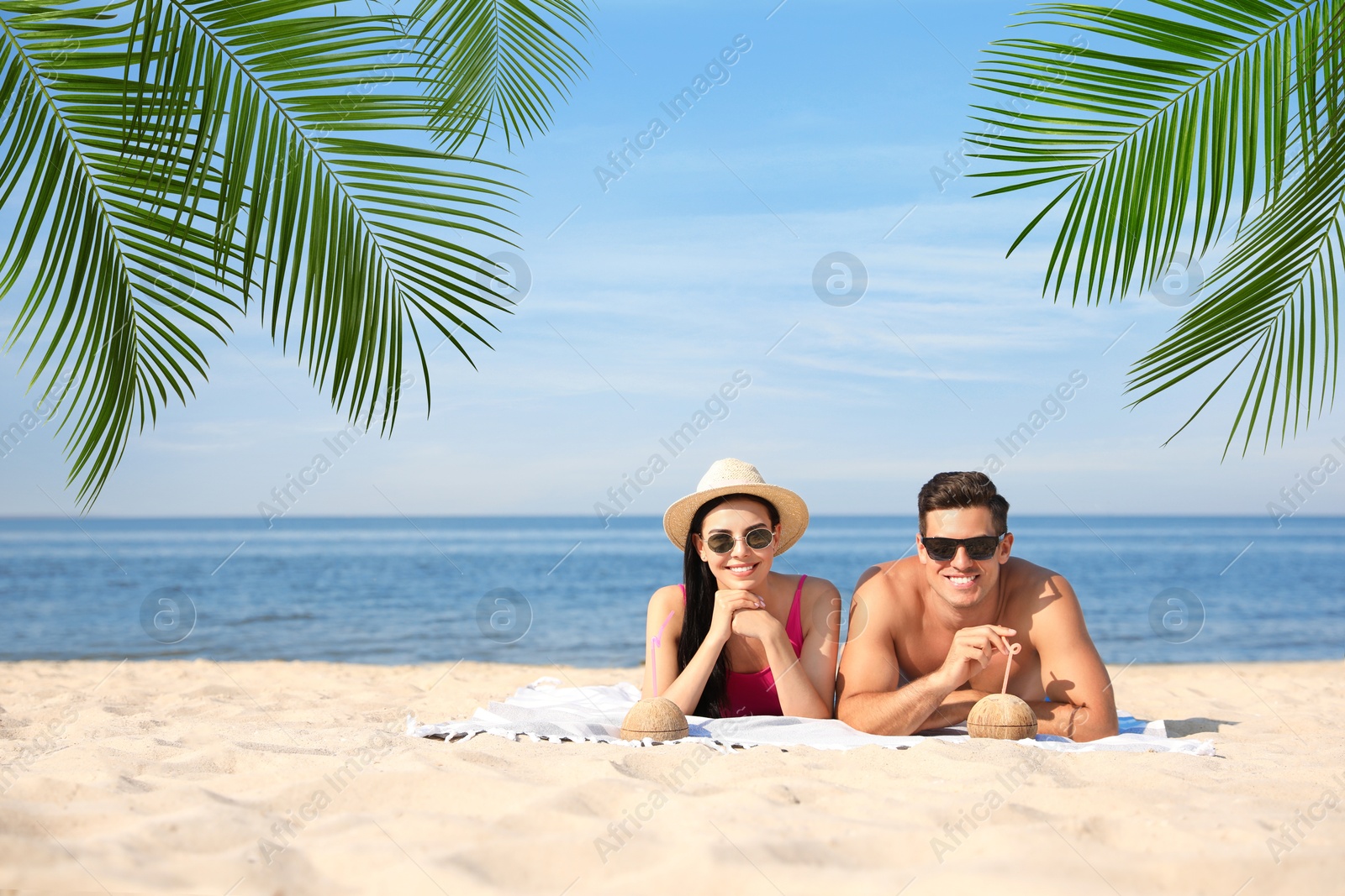 Image of Happy honeymooners relaxing under palm leaves on tropical beach