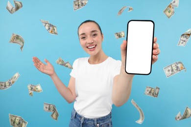 Image of Happy woman showing mobile phone with empty screen under money rain on light blue background