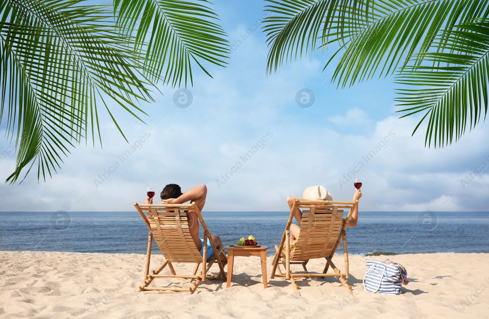 Image of Couple relaxing on deck chairs under palm leaves on tropical beach