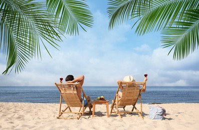 Couple relaxing on deck chairs under palm leaves on tropical beach