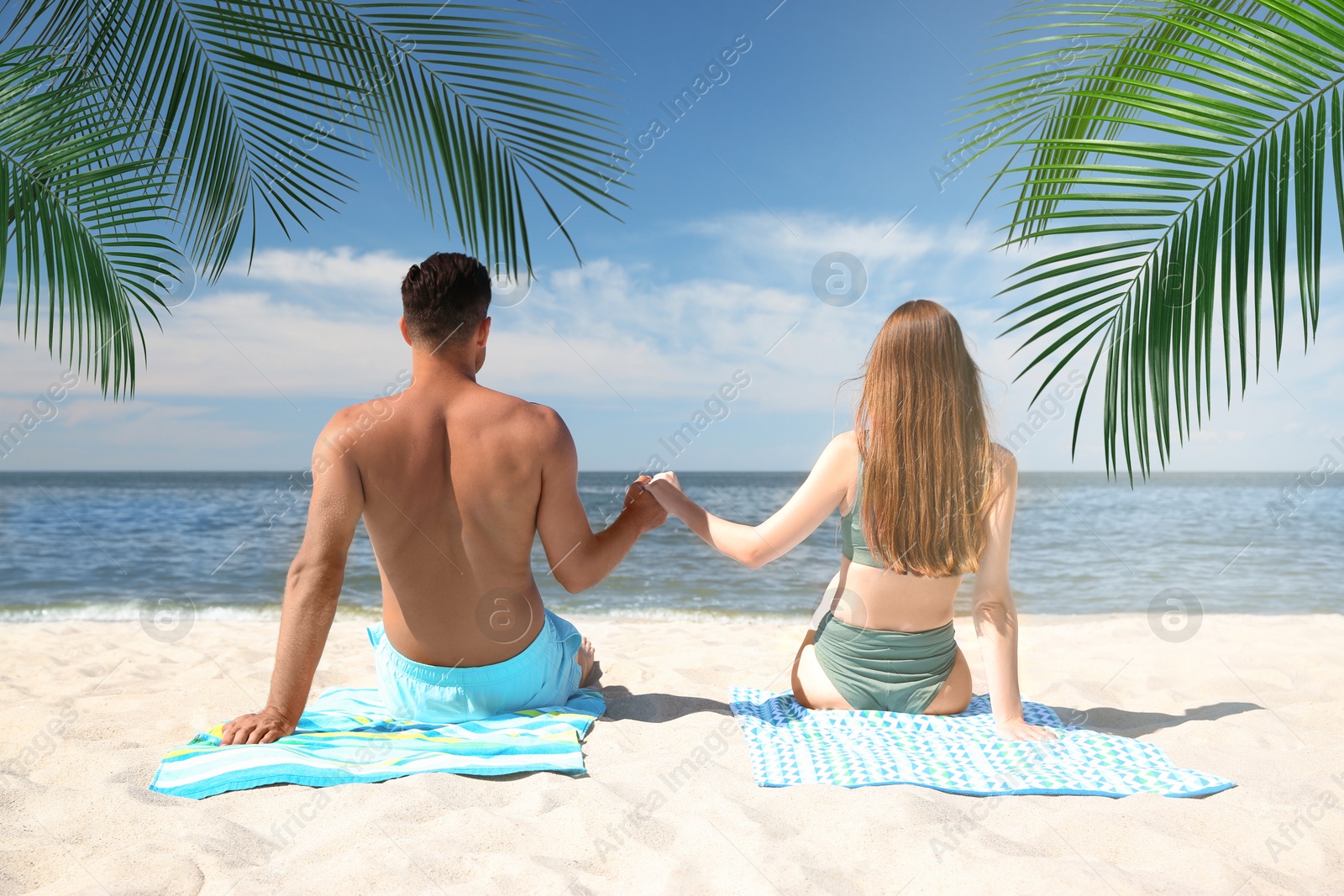 Image of Couple relaxing under palm leaves on tropical beach