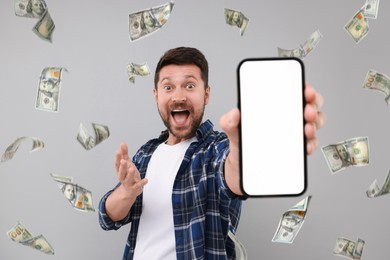 Image of Happy man showing mobile phone with empty screen under money rain on grey background