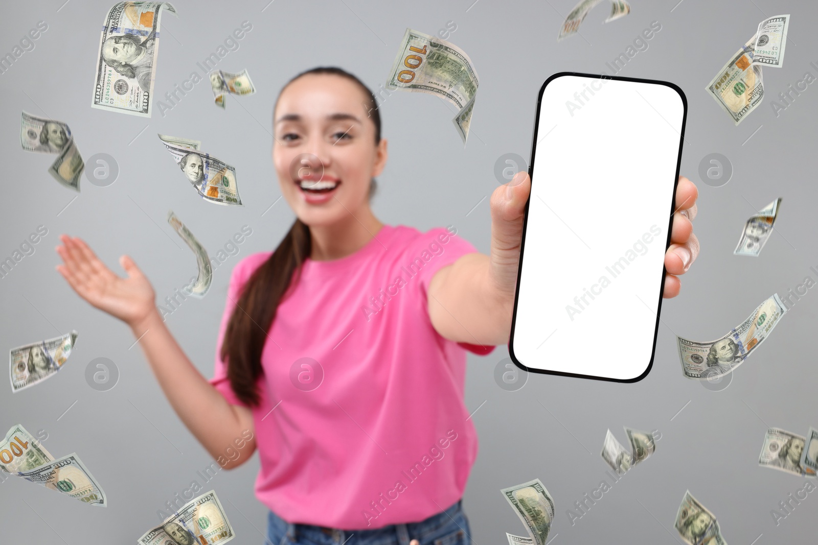 Image of Happy woman showing mobile phone with empty screen under money rain on grey background, selective focus