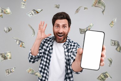 Happy man showing mobile phone with empty screen under money rain on grey background