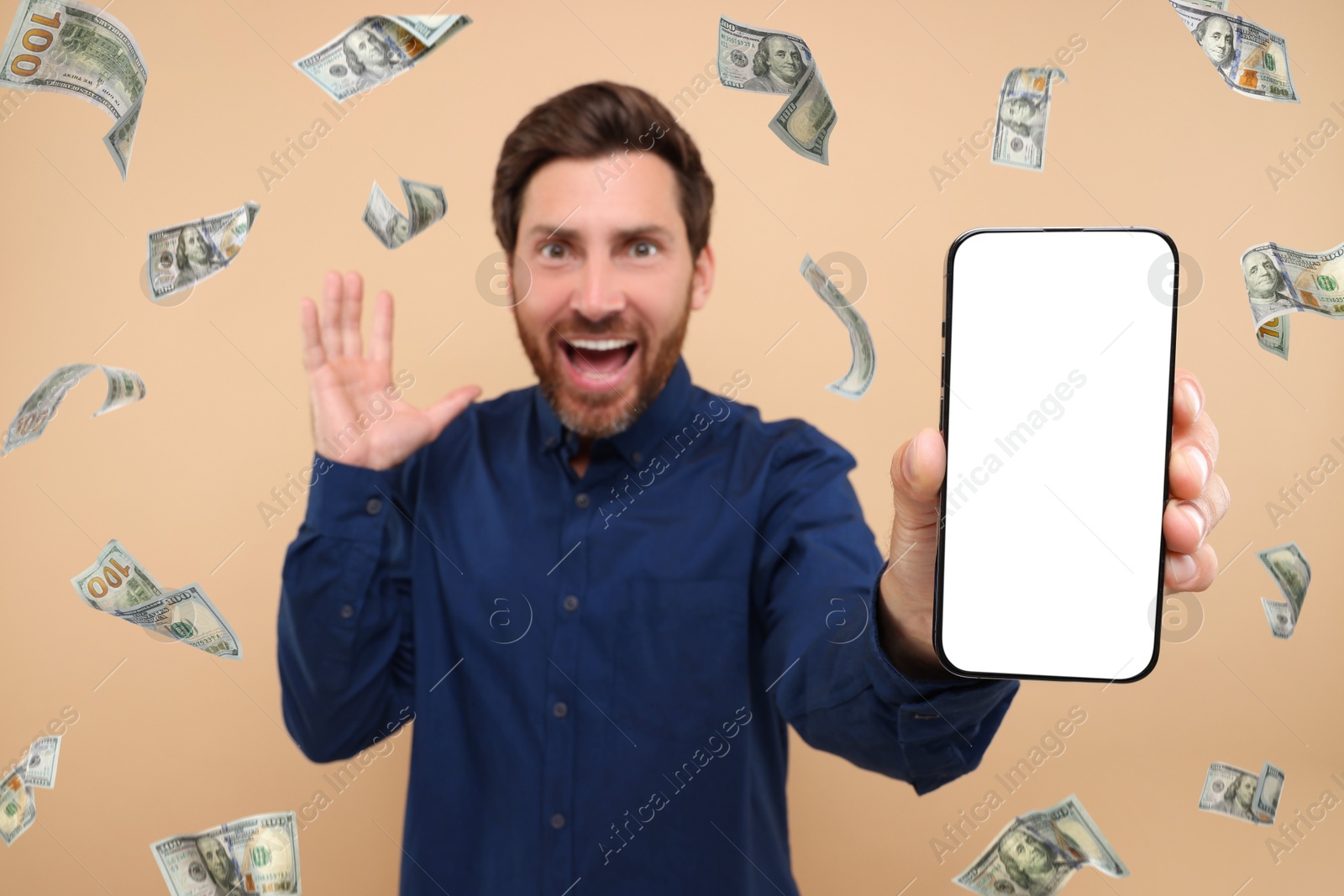 Image of Happy man showing mobile phone with empty screen under money rain on dark beige background, selective focus