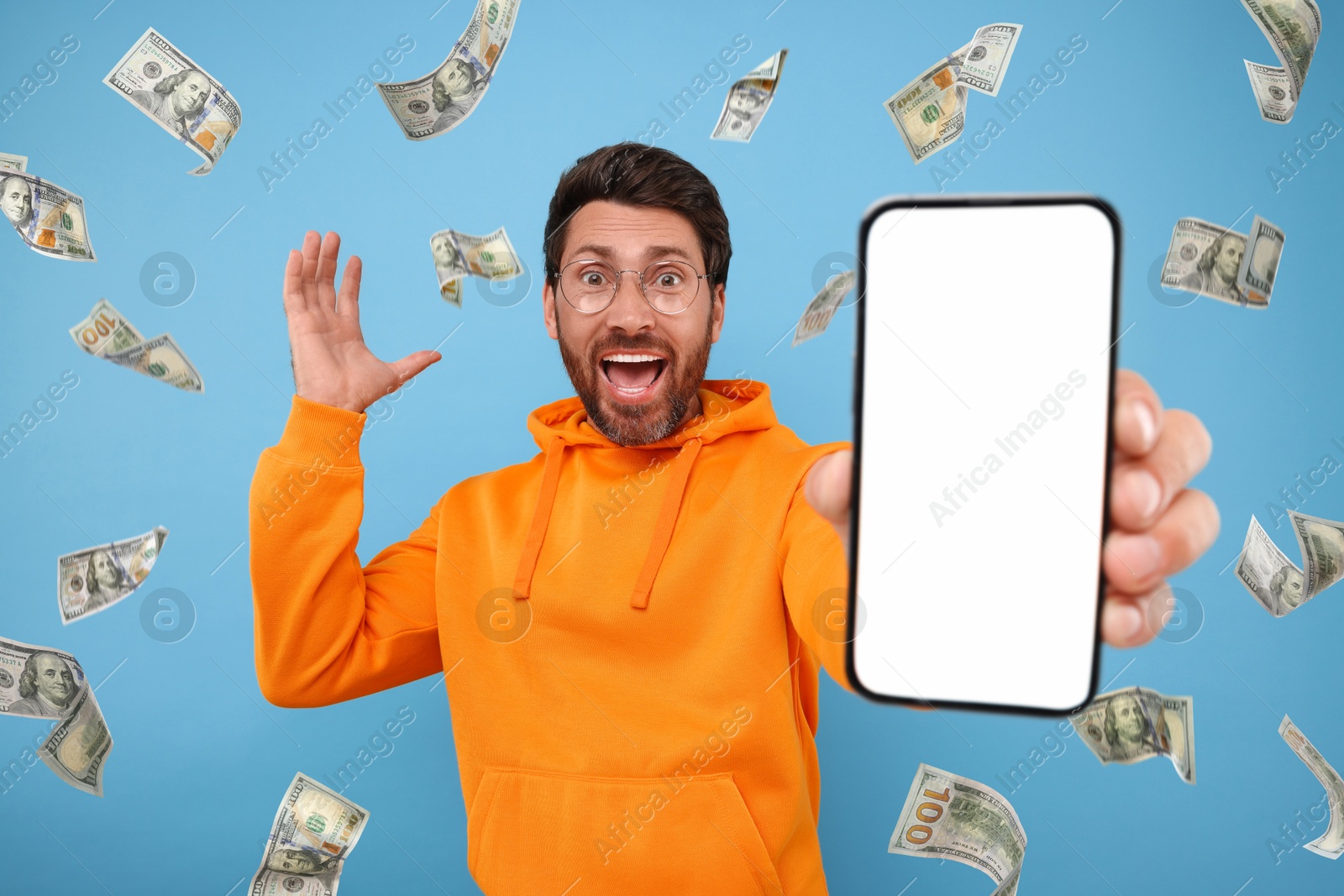 Image of Happy man showing mobile phone with empty screen under money rain on light blue background