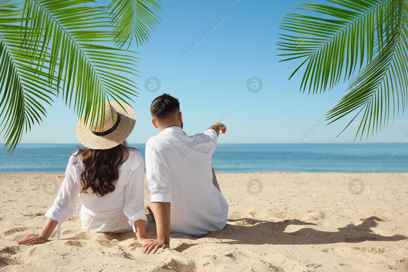 Image of Couple relaxing under palm leaves on tropical beach