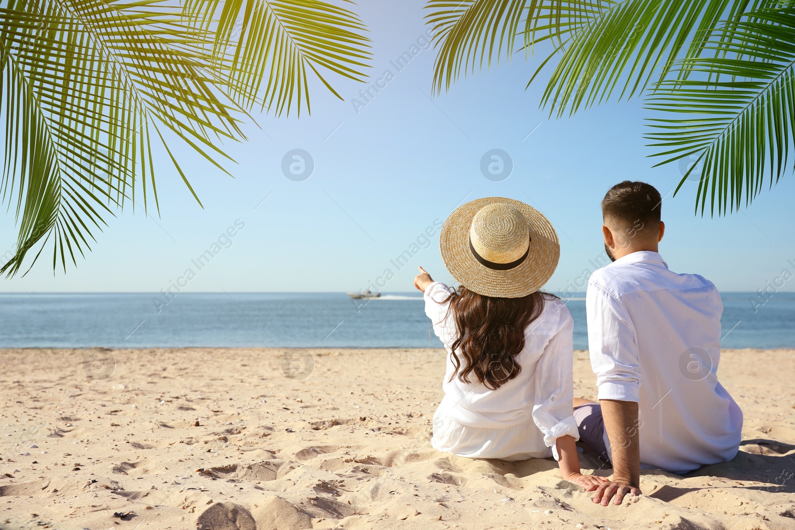 Image of Couple relaxing under palm leaves on tropical beach