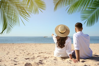 Couple relaxing under palm leaves on tropical beach