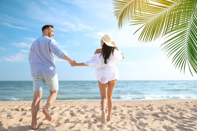 Happy honeymooners walking on sandy beach near sea