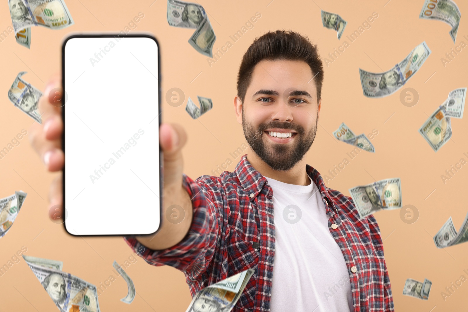 Image of Happy man showing mobile phone with empty screen under money rain on dark beige background