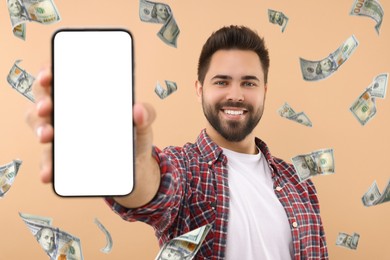 Happy man showing mobile phone with empty screen under money rain on dark beige background