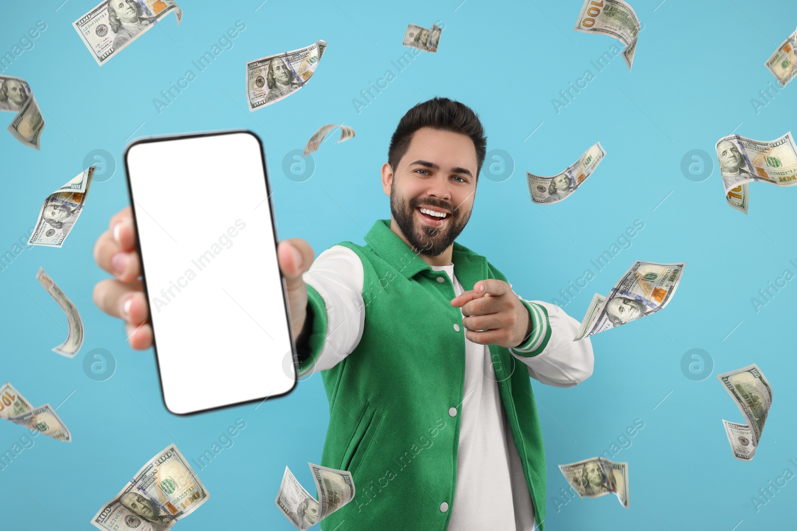 Image of Happy man pointing at mobile phone with empty screen under money rain on light blue background