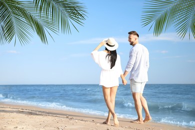 Happy honeymooners walking on sandy beach near sea