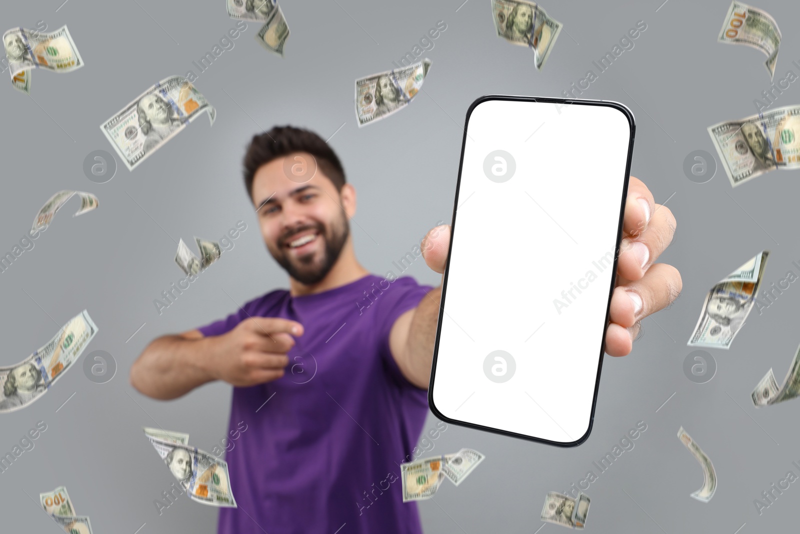 Image of Happy man pointing at mobile phone with empty screen under money rain on grey background, selective focus