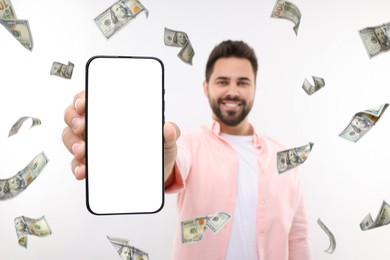 Image of Happy man showing mobile phone with empty screen under money rain on white background, selective focus