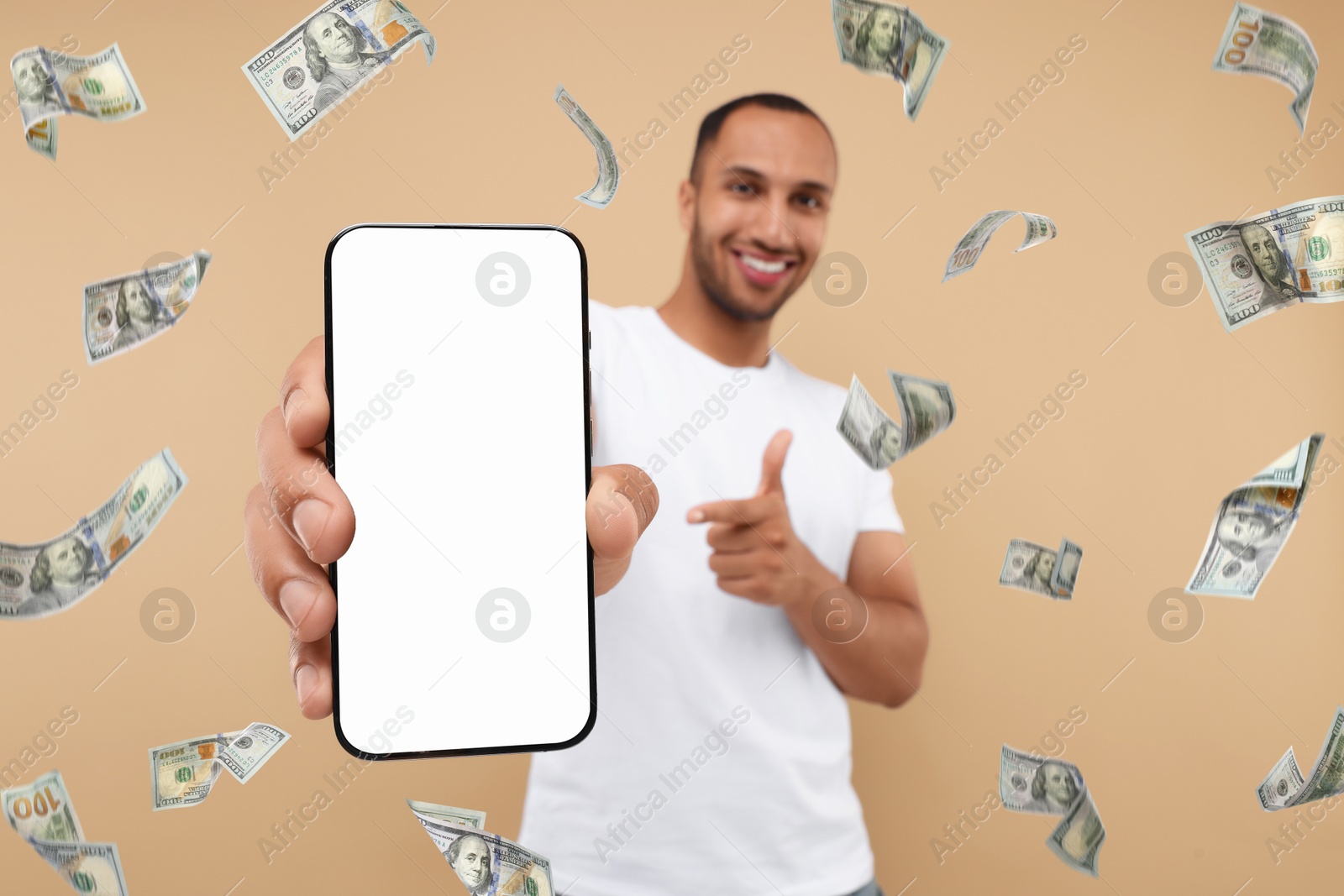 Image of Happy man pointing at mobile phone with empty screen under money rain on dark beige background, selective focus