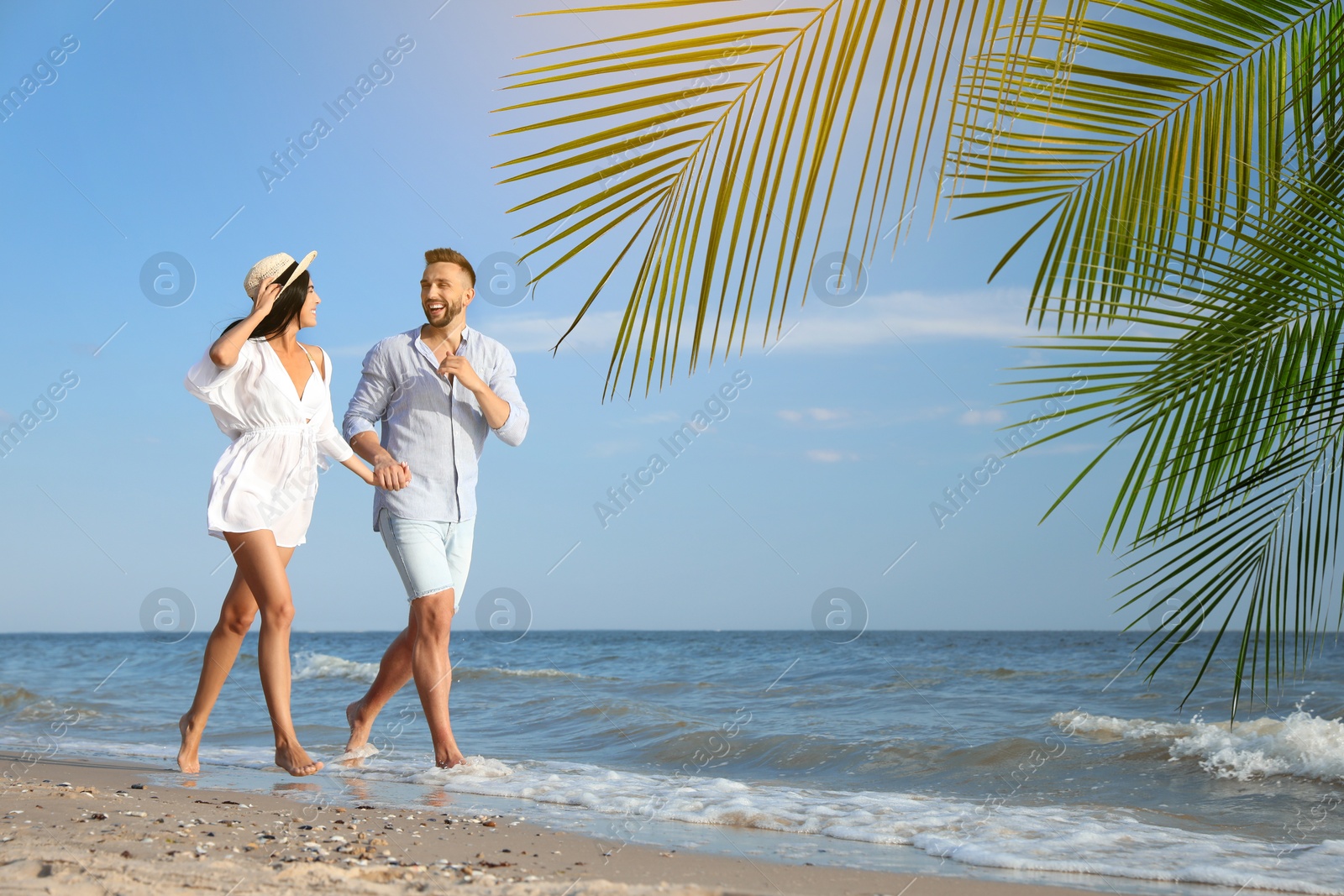 Image of Happy honeymooners walking on sandy beach near sea