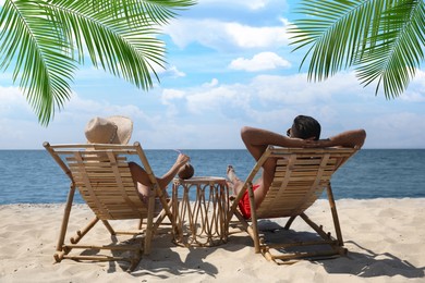 Couple relaxing on deck chairs under palm leaves on tropical beach