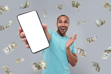 Happy man showing mobile phone with empty screen under money rain on grey background