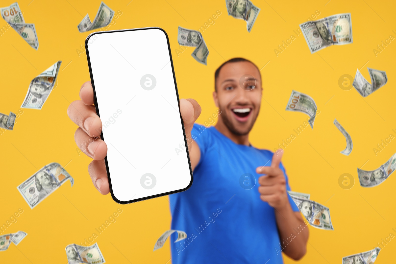 Image of Happy man pointing at mobile phone with empty screen under money rain on orange background, selective focus