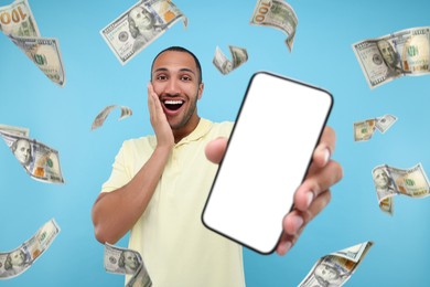 Happy man showing mobile phone with empty screen under money rain on light blue background