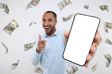 Happy man pointing at mobile phone with empty screen under money rain on white background