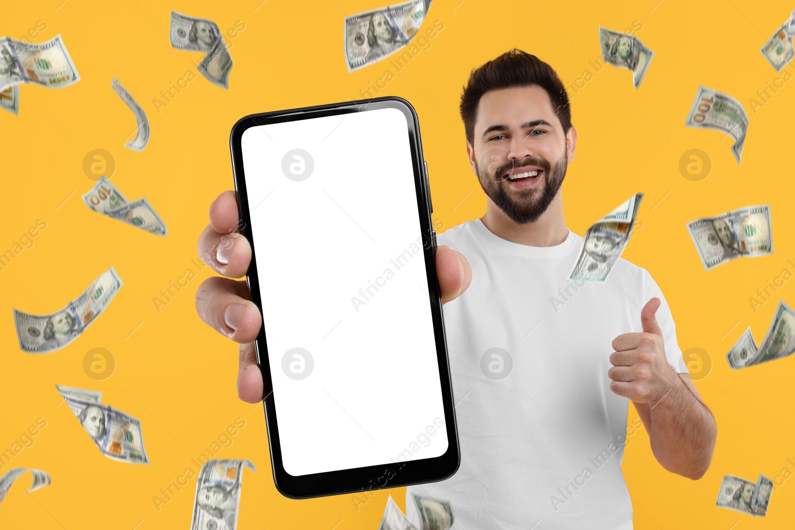 Image of Happy man showing mobile phone with empty screen under money rain on orange background