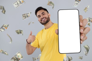 Image of Happy man showing mobile phone with empty screen under money rain on grey background