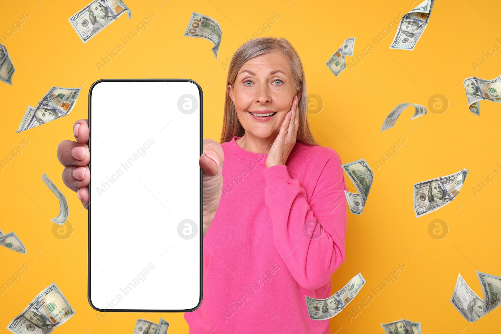 Image of Happy woman showing mobile phone with empty screen under money rain on orange background