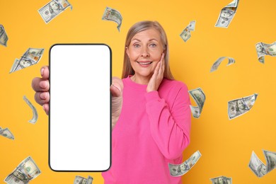 Happy woman showing mobile phone with empty screen under money rain on orange background