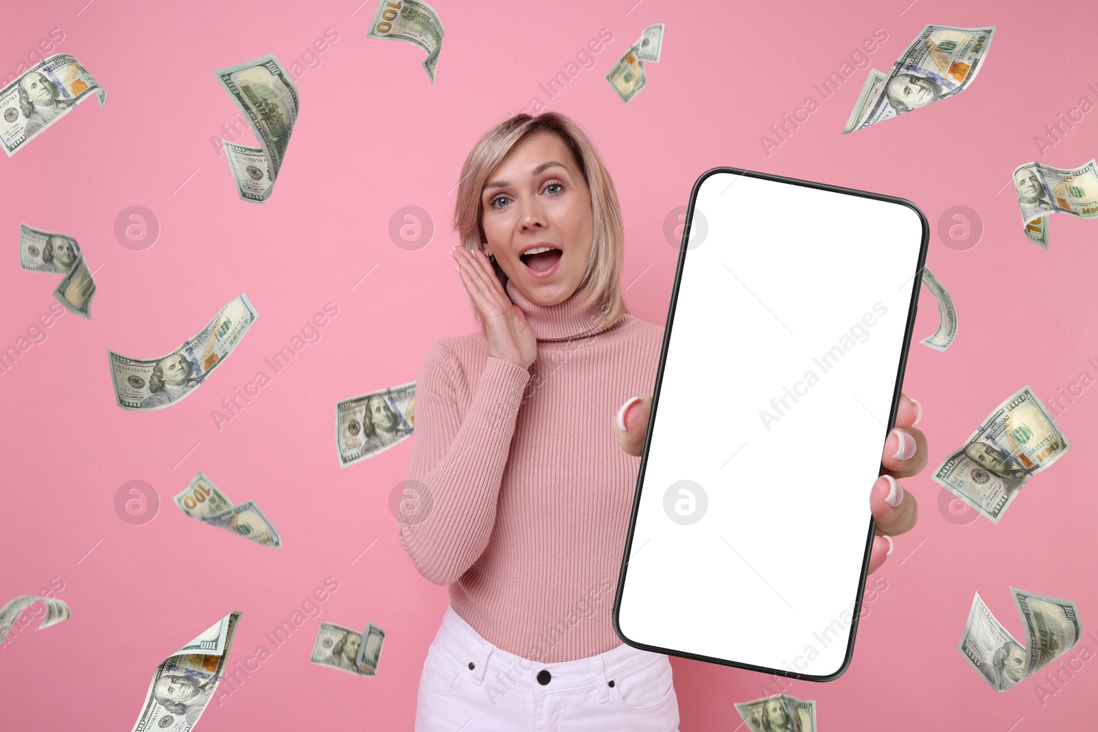 Image of Surprised woman showing mobile phone with empty screen under money rain on pink background