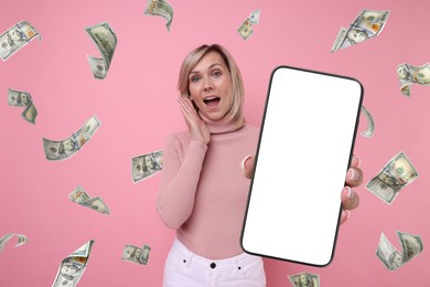 Surprised woman showing mobile phone with empty screen under money rain on pink background