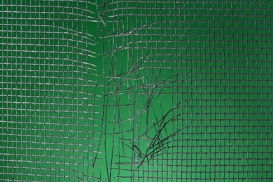 Torn window screen against green background, closeup