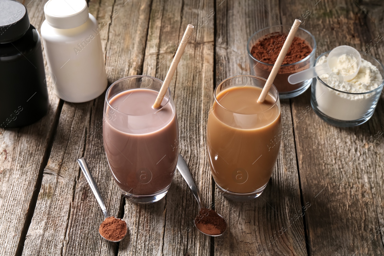 Photo of Delicious protein shakes in glasses, powder, spoons and plastic bottles on wooden table