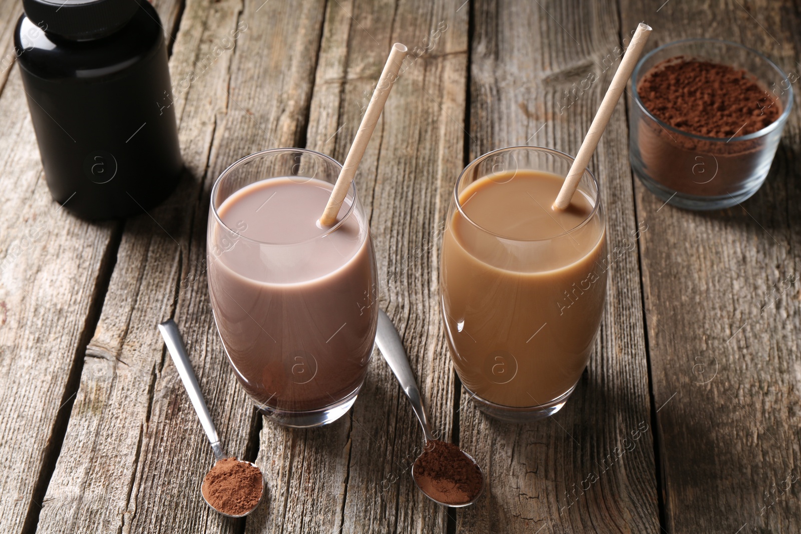 Photo of Delicious protein shakes in glasses, powder, spoons and plastic bottle on wooden table