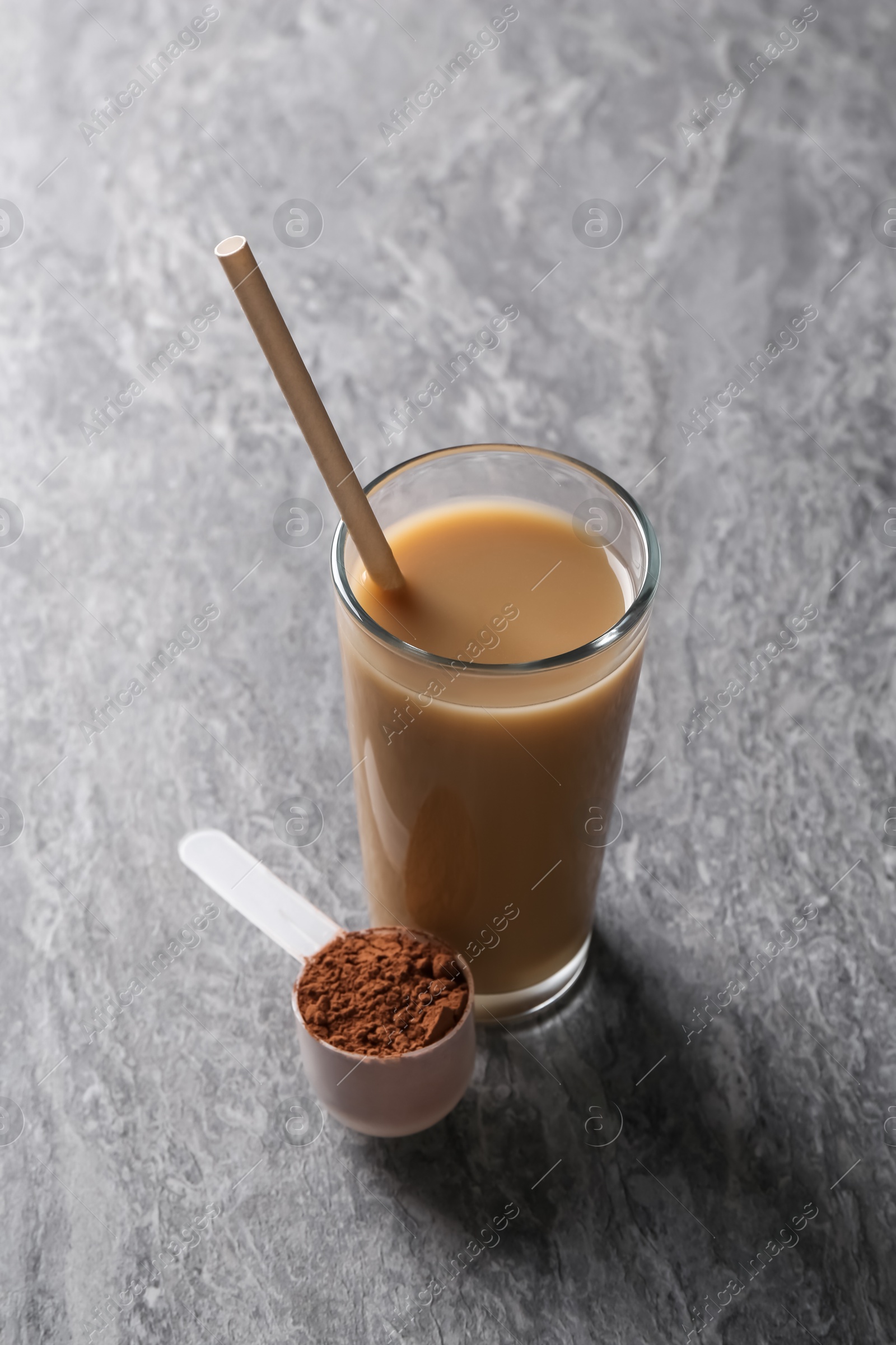 Photo of Delicious protein shake in glass and scoop with powder on grey table