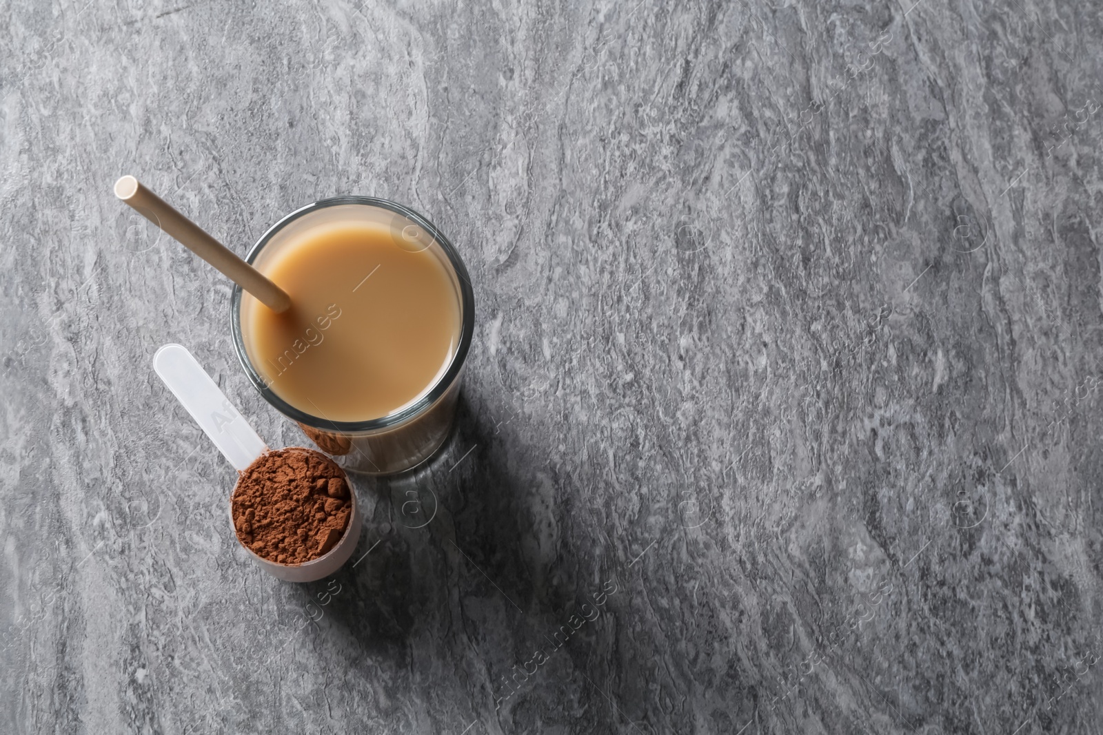 Photo of Delicious protein shake in glass and scoop with powder on grey table, top view. Space for text