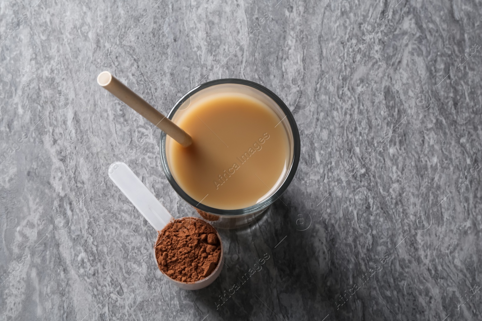 Photo of Delicious protein shake in glass and scoop with powder on grey table, top view