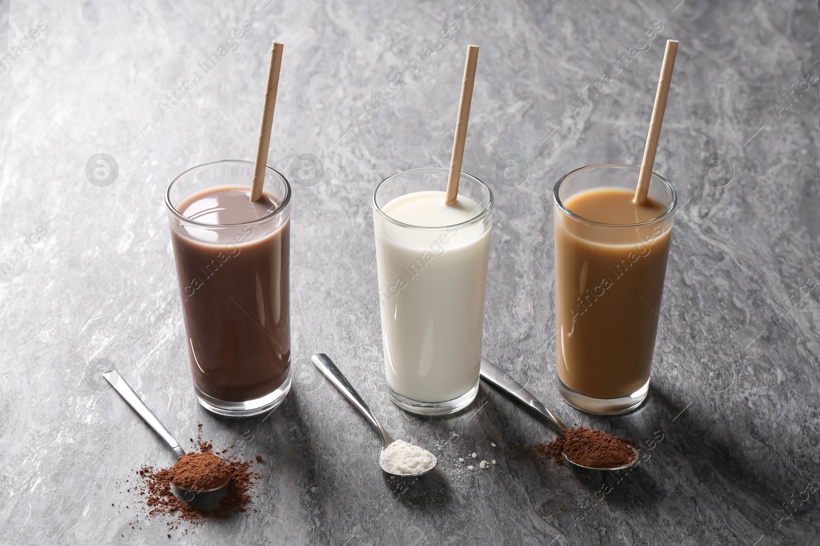 Photo of Delicious protein shakes in glasses and spoons with powder on grey table