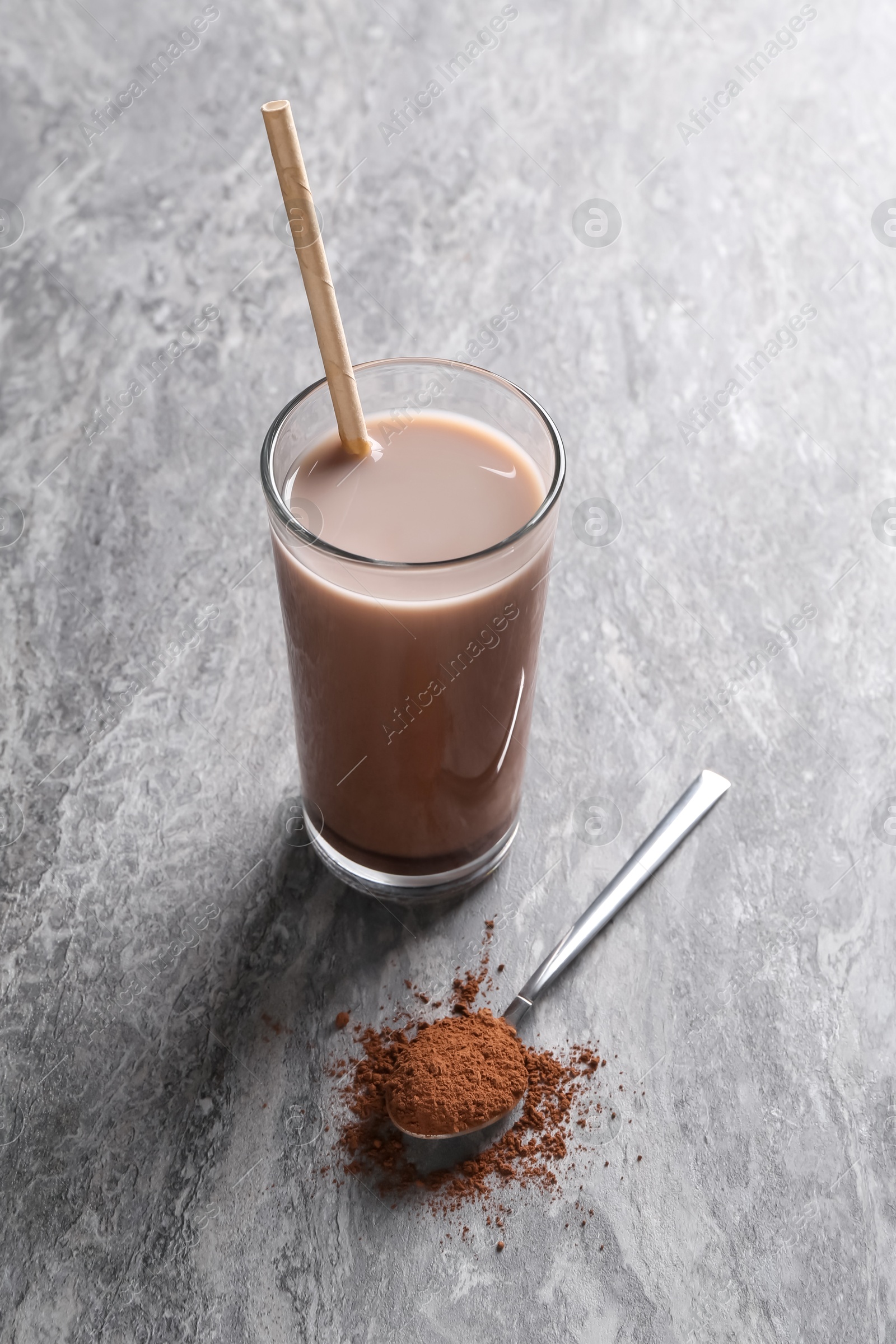 Photo of Delicious protein shake in glass and spoon with powder on grey table