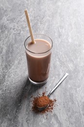 Photo of Delicious protein shake in glass and spoon with powder on grey table