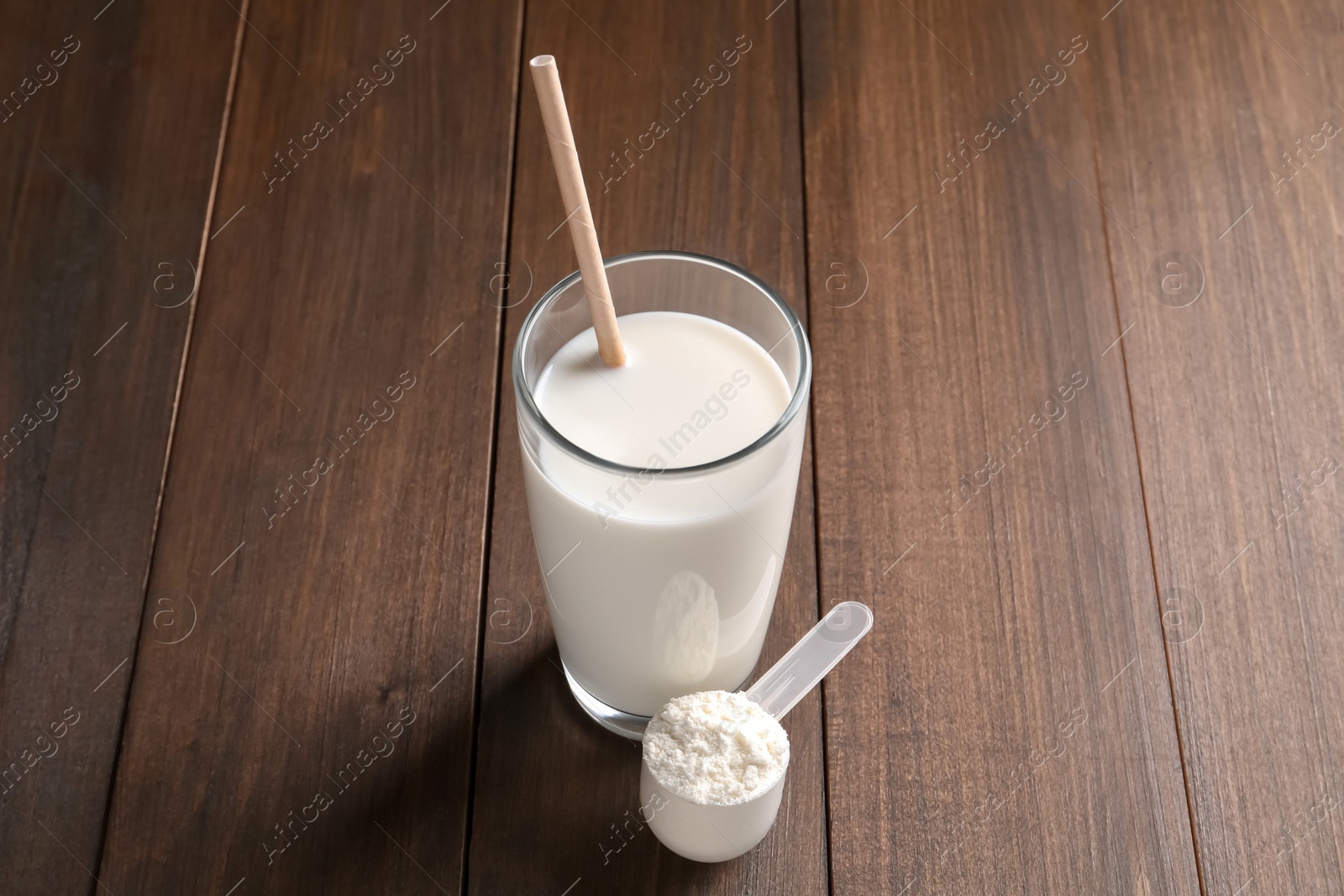 Photo of Delicious protein shake in glass and scoop with powder on wooden table