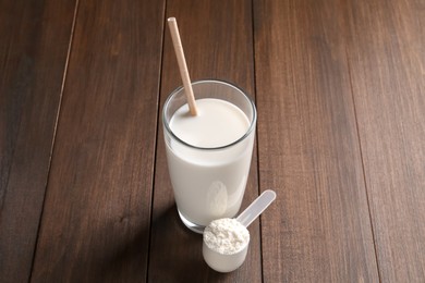 Photo of Delicious protein shake in glass and scoop with powder on wooden table